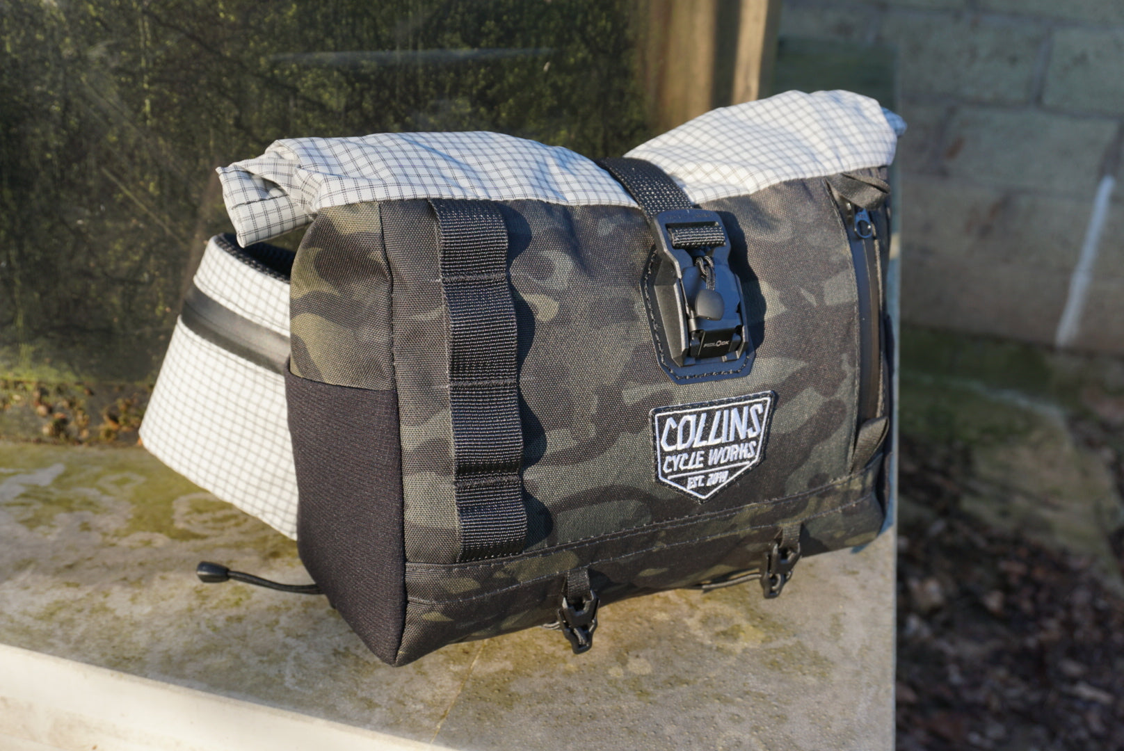 Camouflage bag with plaid top section on a stone surface